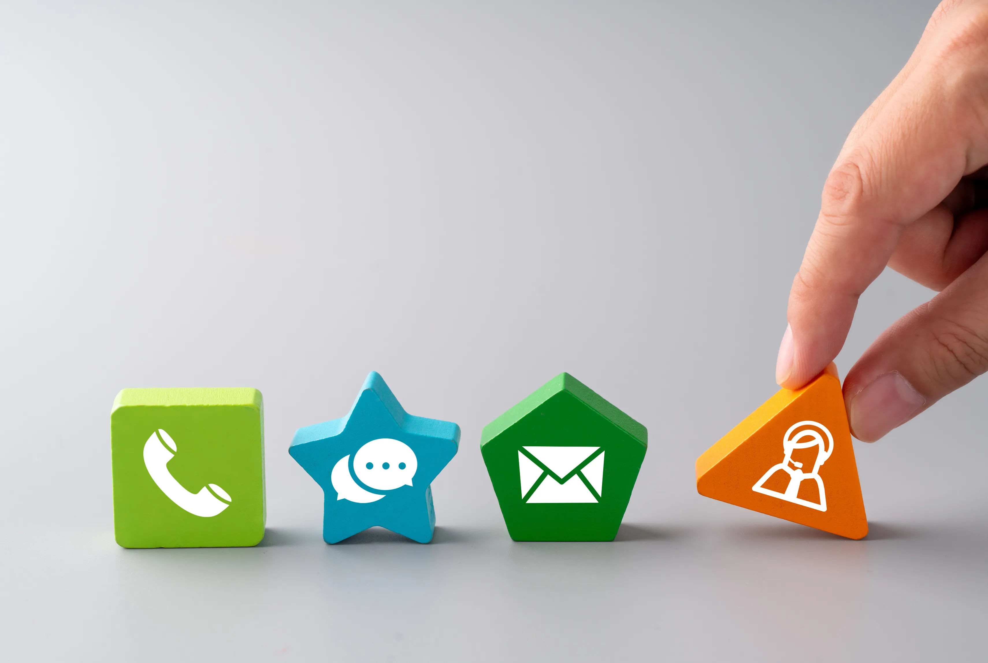 Colourful wooden shapes showing a telephone, message, envelope and support icons on a plain background.