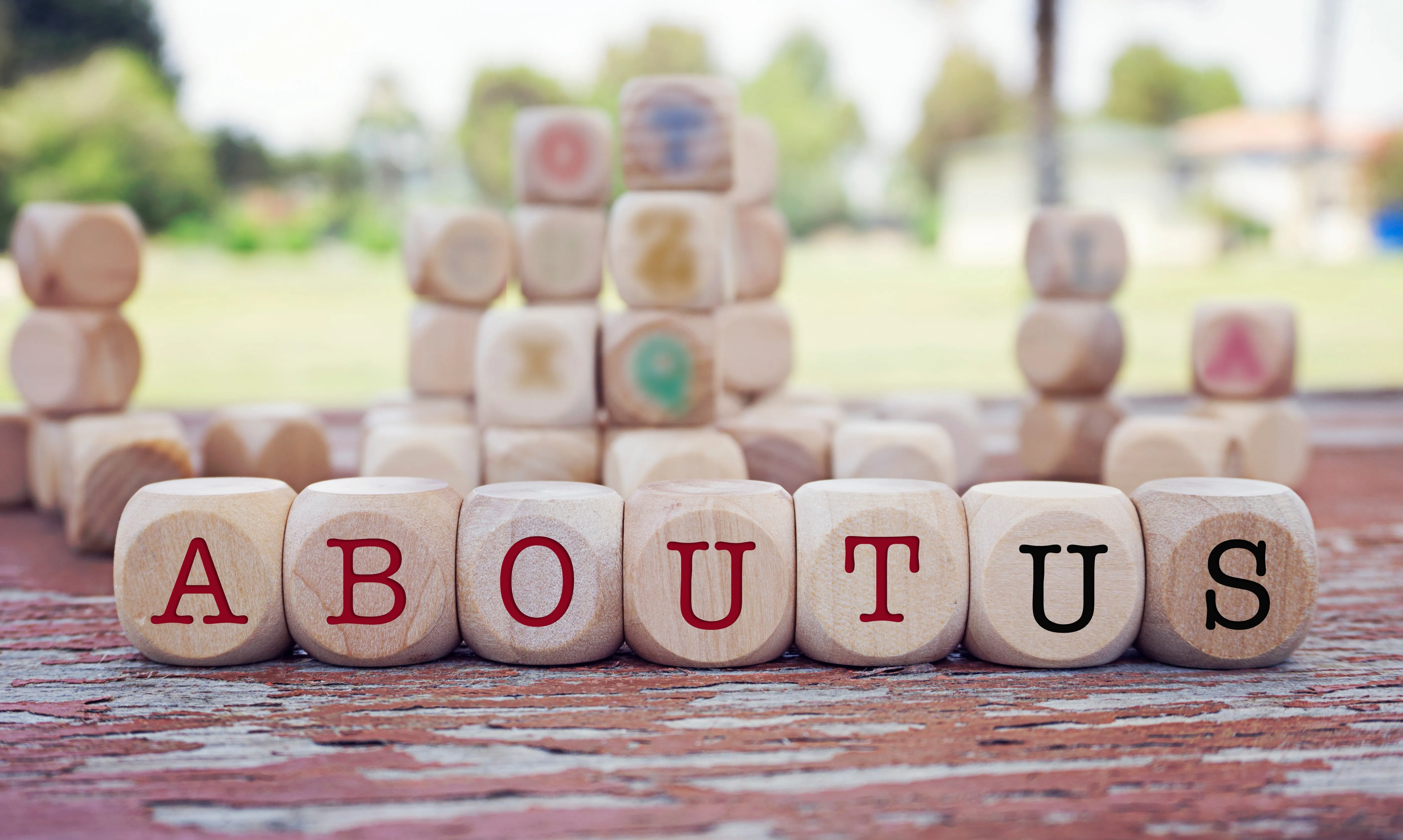 Wooden letter blocks arranged in a row on a table outdoors, with more blocks stacked behind them.