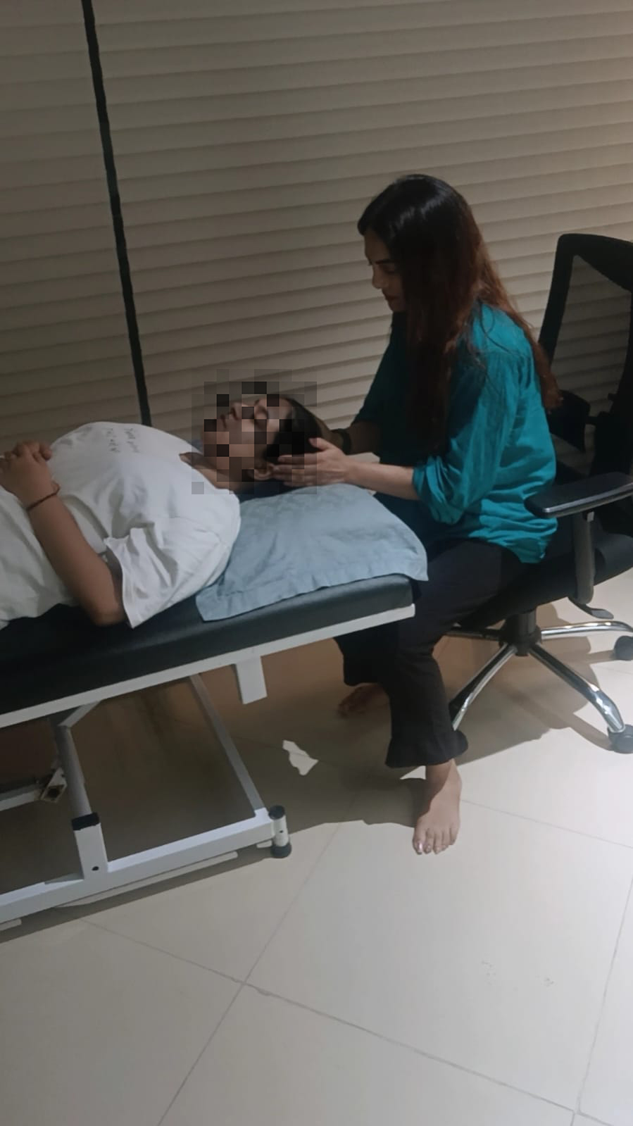 A one-to-one session in a quiet room: a person rests on a treatment couch while Vibha Jain sits alongside them.
