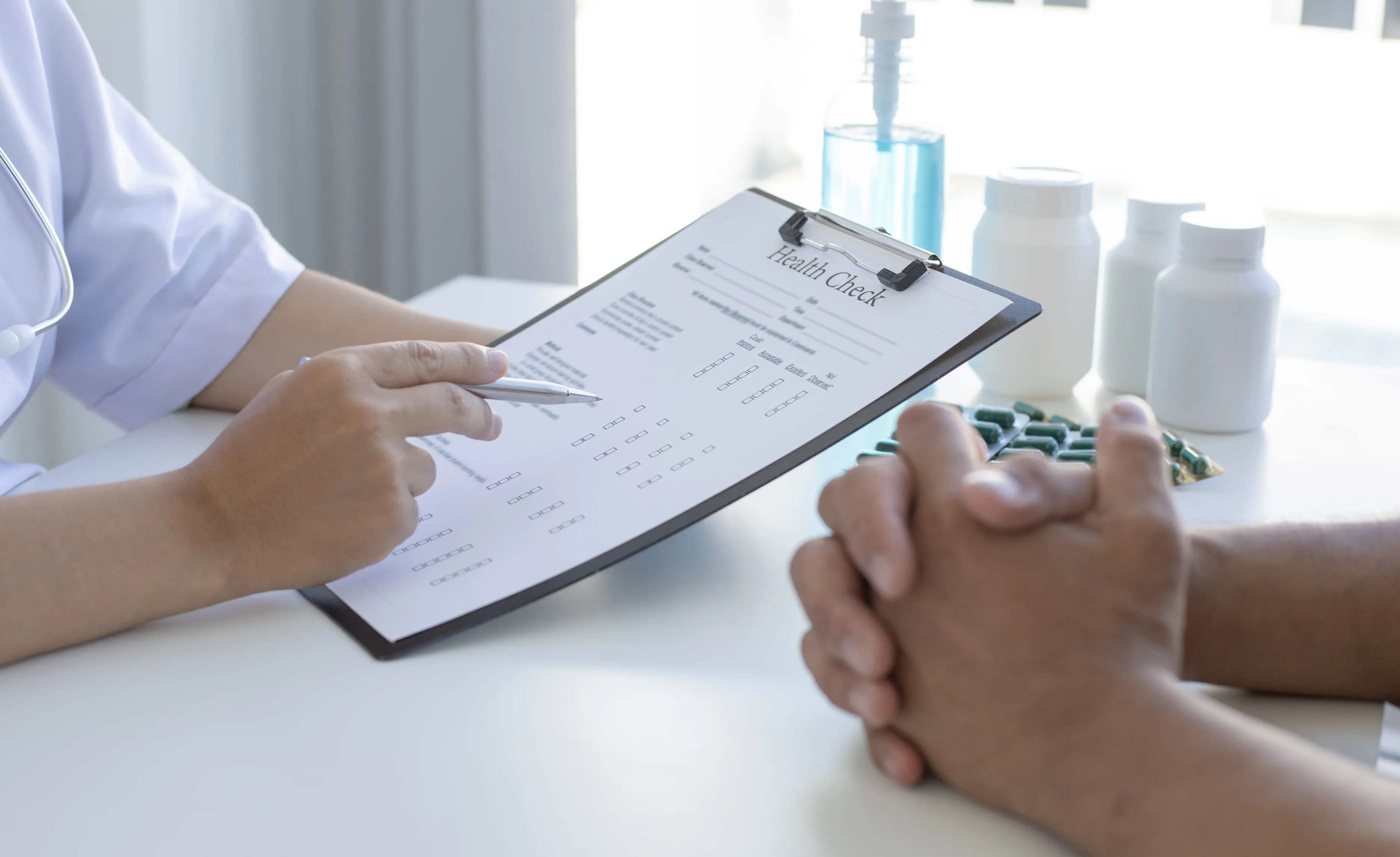 A healthcare professional holding a health check form while talking with a seated person.