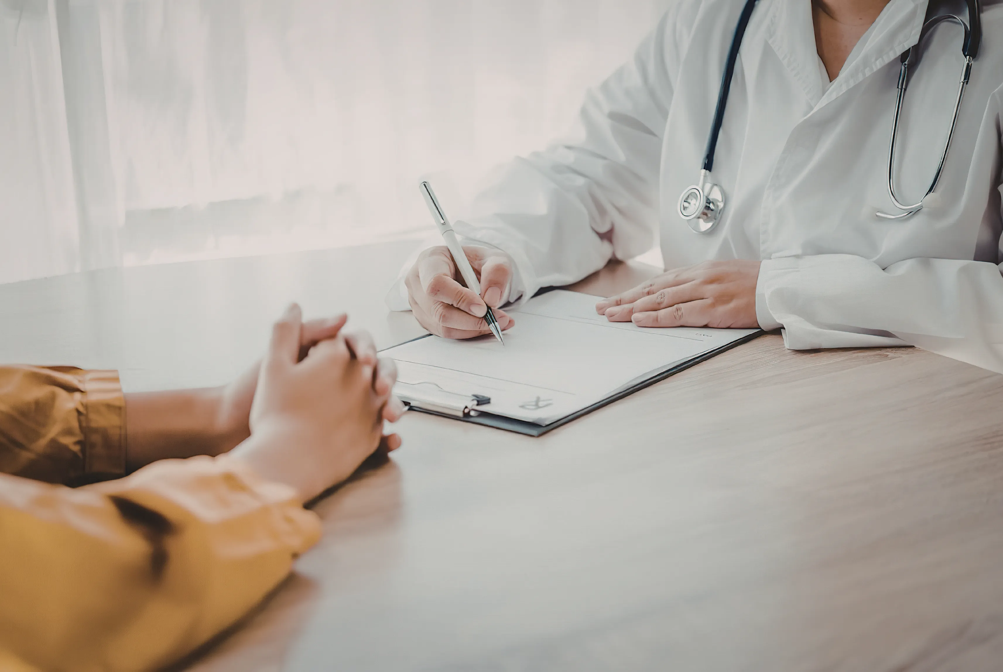 A parent sitting across a desk from a healthcare professional who is making notes during a consultation.